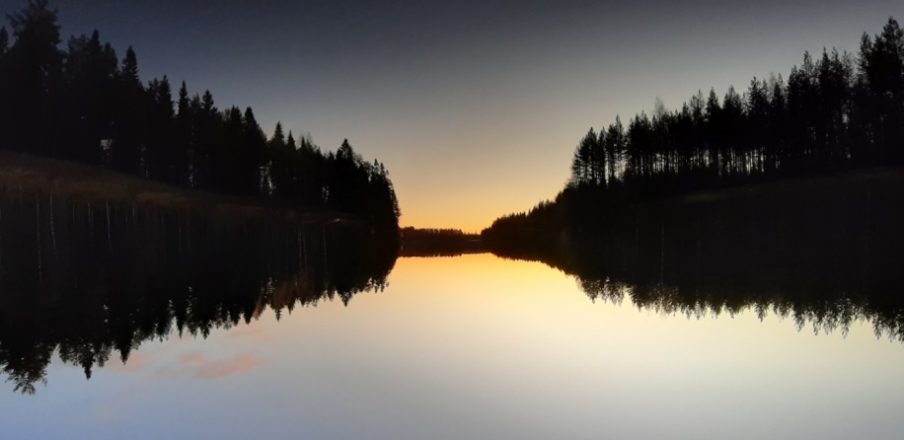 Emäjoen tyyni vedenpinta Ämmän voimalaitoksen alapuolella heijastaa rannan puut ja laskevan auringon säteet lokakuussa 2019. 