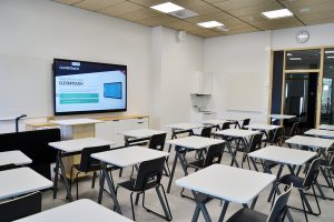 Koululuokkatila, useita pöytiä ja tuoleja niiden takana, seinustalla iso älynäyttö, jossa on teksti clevertouch. luokassa ei ole ihmisiä.